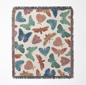 Faith-inspired woven blanket with hand-drawn butterflies and moths on a soft light background, made from 100% cotton with colorful fringed edges—Christian home decor.
