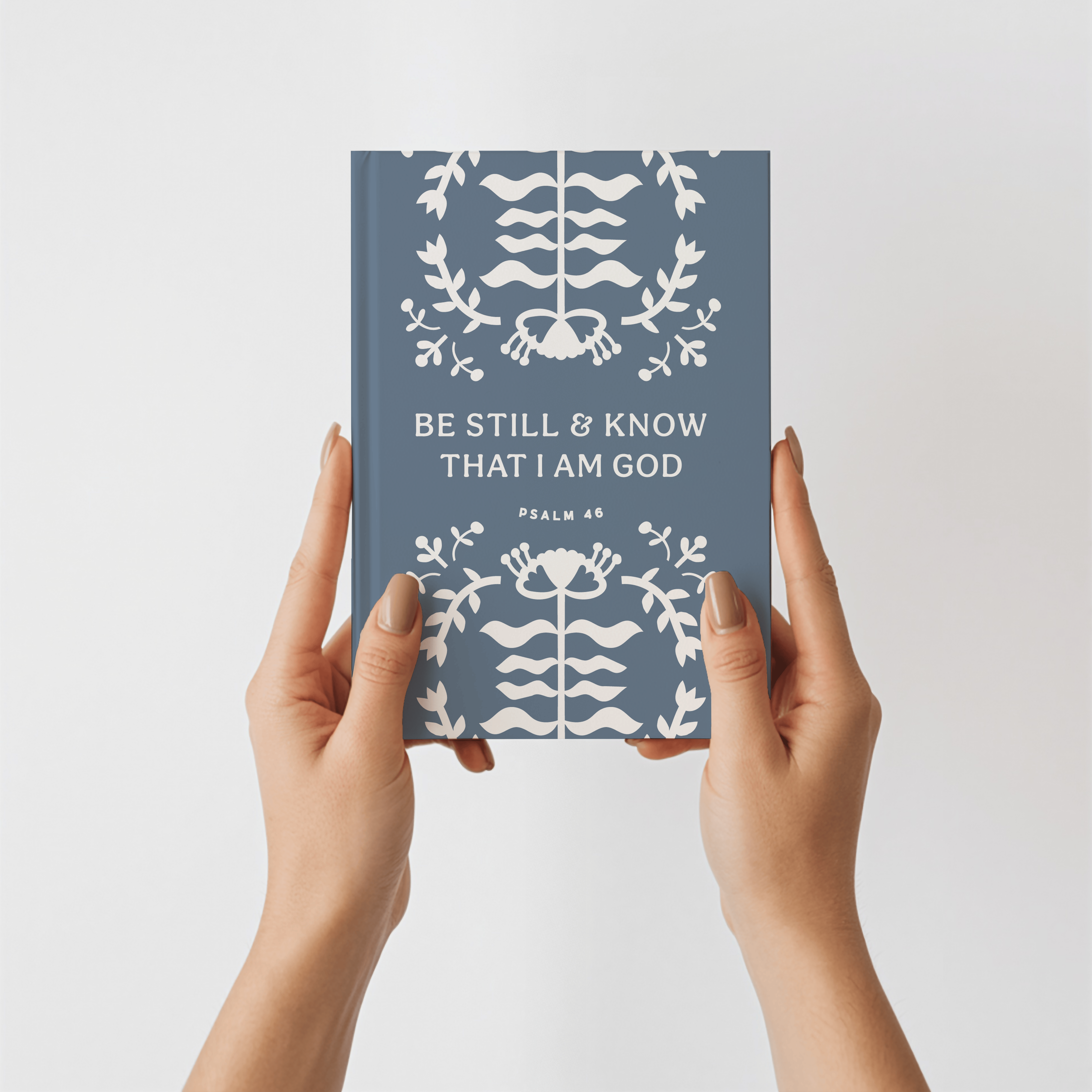 Book titled 'Be Still & Know That I Am God' held by hands against a light gray background