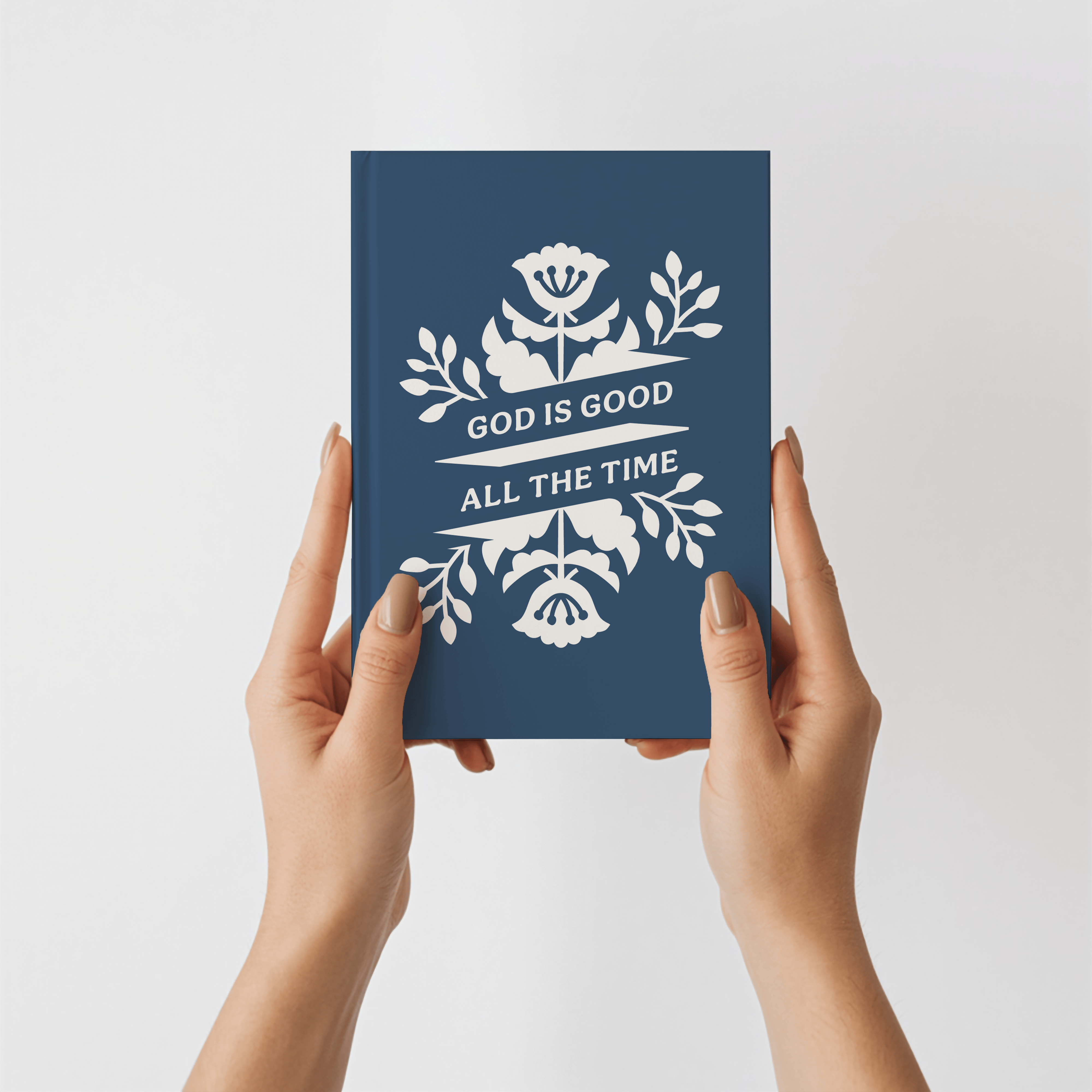Navy blue book with white floral design and text held by hands against a light gray background