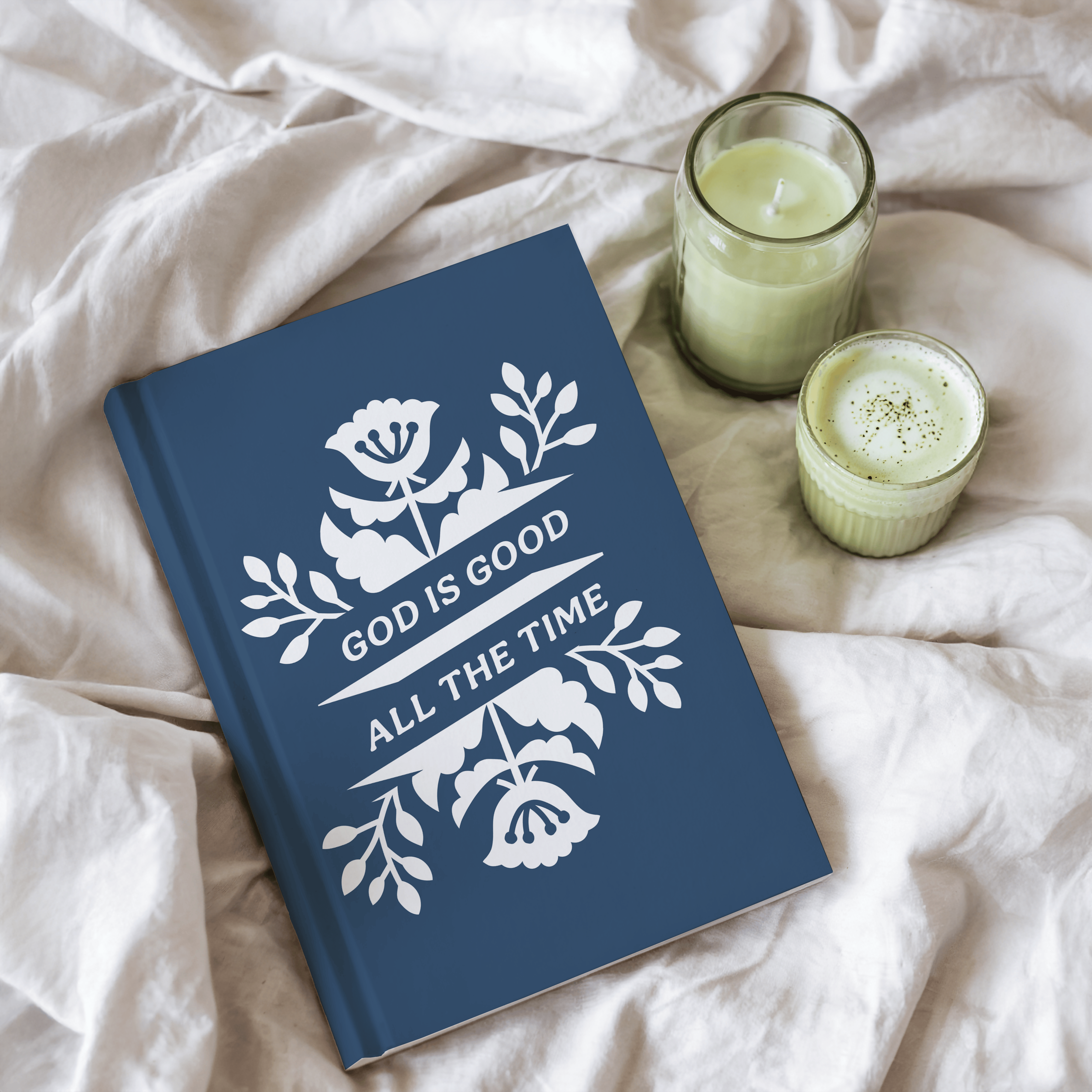 Blue book with 'God is Good All the Time' quote on a white fabric background with two candles.