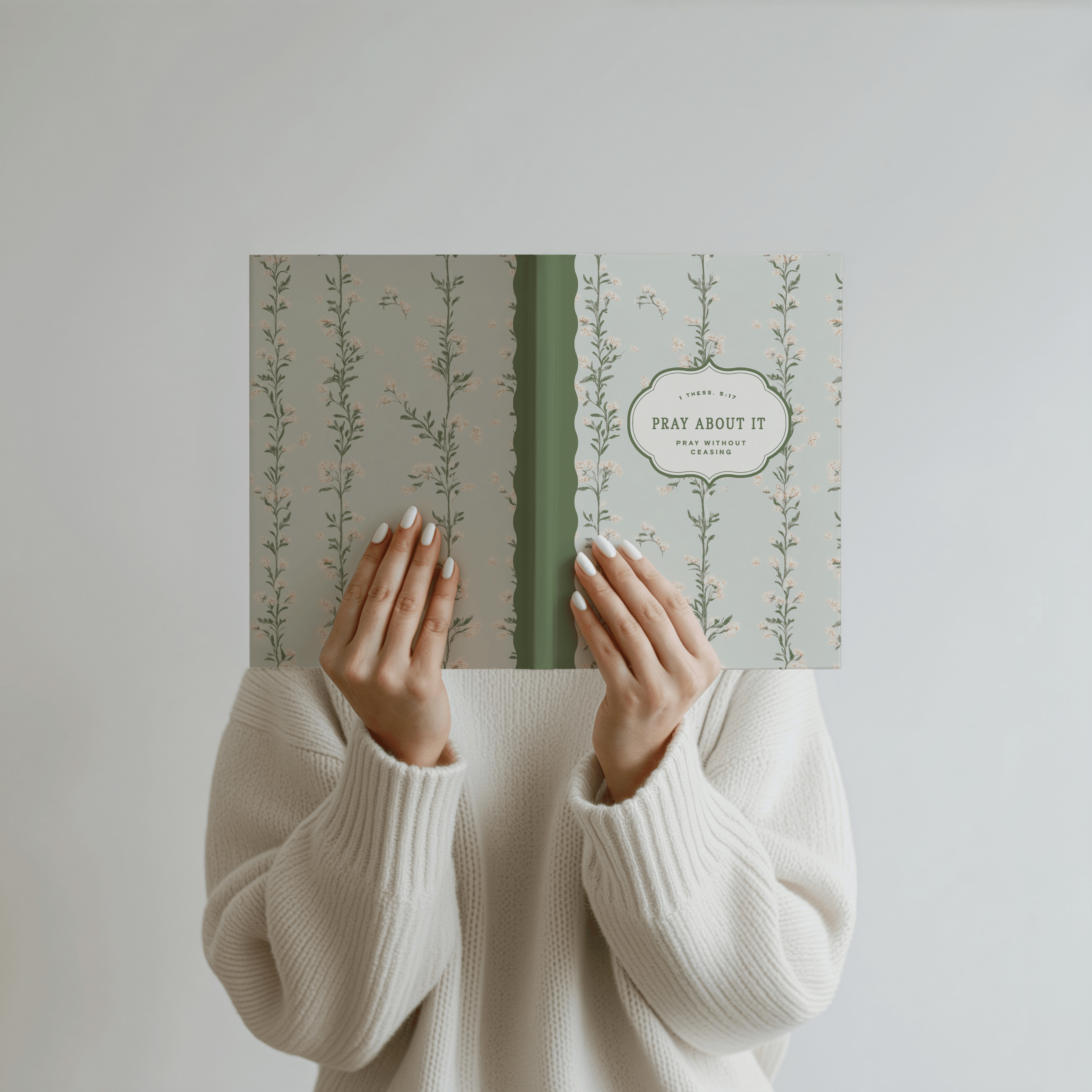 Person wearing a white sweater holding a green notebook with floral design and text.